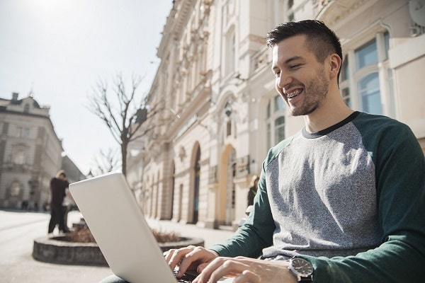 Young college student with braces studying on his laptop outside