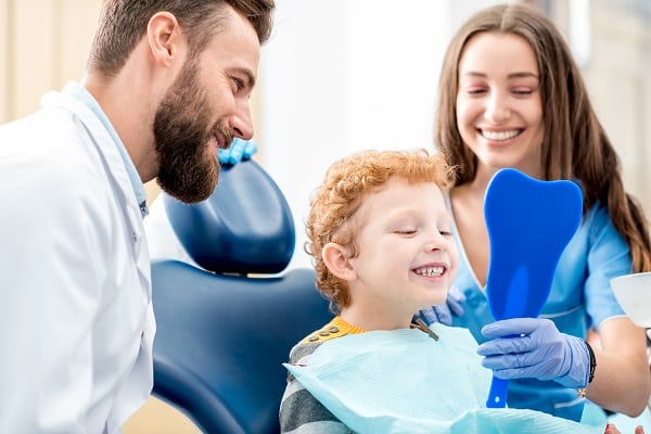 Young boy who just got his braces off seated next to father and orthodontic assistant