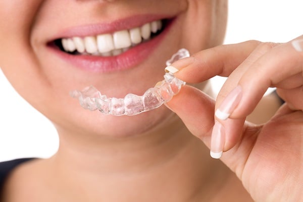 Invisalign aligner being held close up in front of a woman's smile