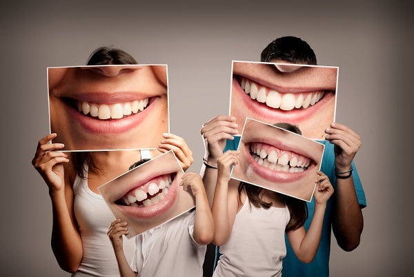 A family of four holding close-up photos of their smiles up to their faces