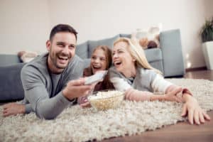 Fathermother and daughter lying on floorwatching TV and eating popcorn.