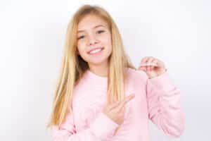 Cute young girl smiling while holding Invisalign aligner in one hand in Denver, CO