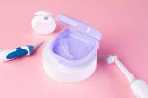 Close up shot of a set of retainers in their case with an electric toothbrush and a pick for cleaning.