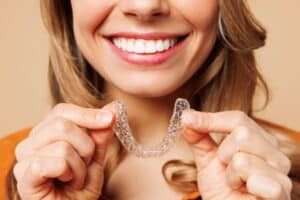 A close-up shot of a woman smiling and holding an Invisalign aligner