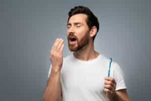 A man with Incognito™ braces holding a toothbrush and testing his breath