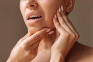 A woman holding her misaligned jaw and considering orthognathic surgery in Denver