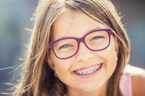 Happy smiling girl with dental braces and glasses. Young cute caucasian blond girl wearing teeth braces and glasses 1766076383 braces young student 1 Orthodontics in Denver CO