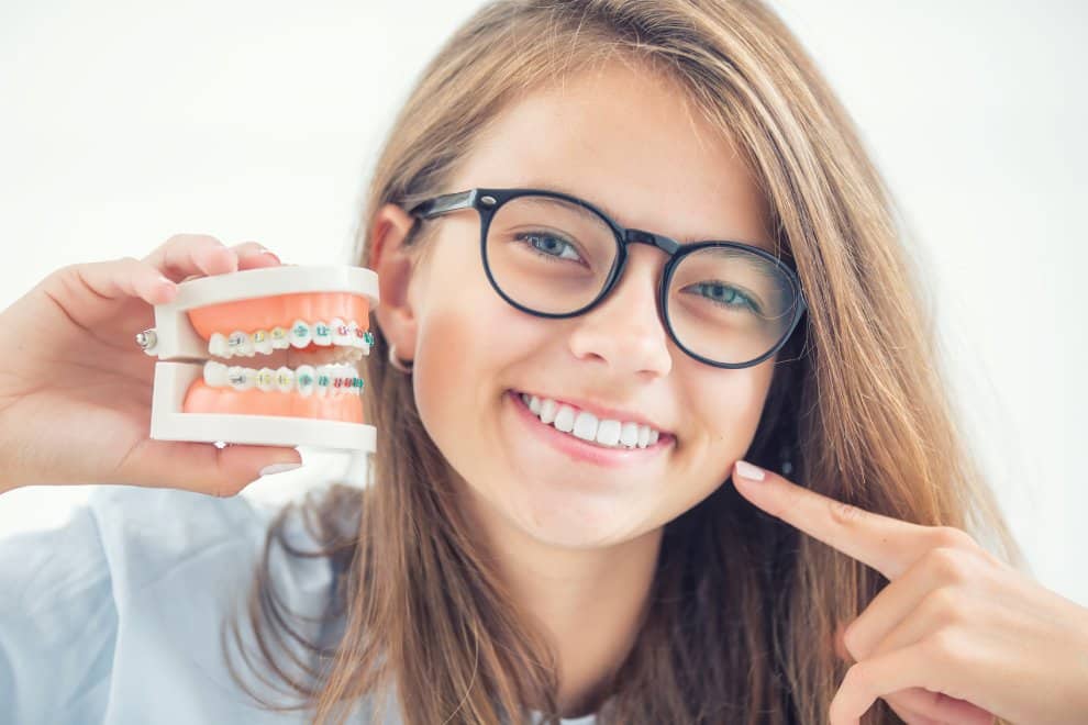 Teen smiling with a braces model, representing orthodontic treatment timelines