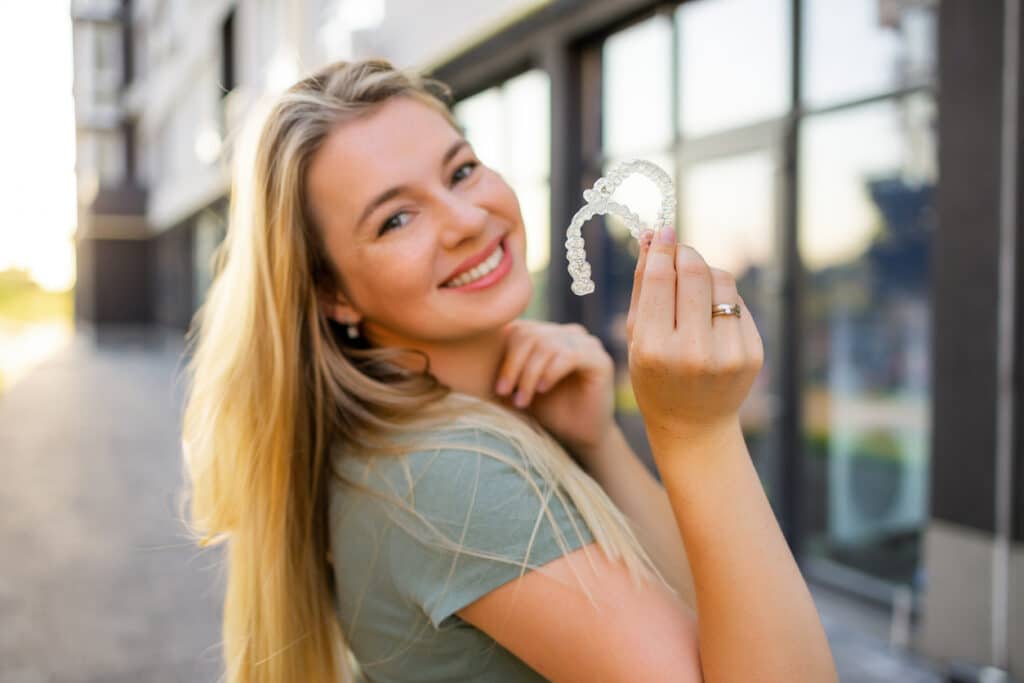 Smiling woman holding clear orthodontic retainers after completing braces or Invisalign treatment.